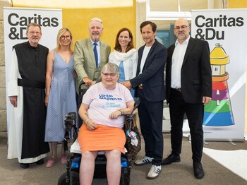 Gruppenfoto vor zwei „Caritas & Du“-Bannern: Mehrere Personen stehen zusammen, in der Mitte sitzt eine Person im Rollstuhl 