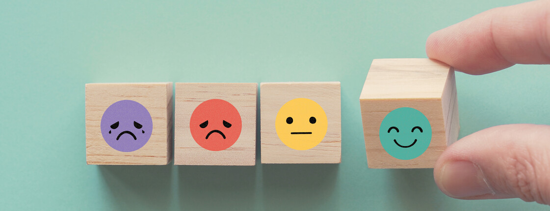 Hand wählt einen Holzblock mit fröhlichem Smiley, Symbol für positives Feedback, gute Bewertungen und psychisches Wohlbefinden.
