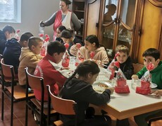 Eine Gruppe Kinder sitzt an einem Tisch und isst. Der Tisch ist mit Nikolausdekorationen geschmückt. 