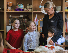 Kinder stehen vor einem Regal mit Spielsachen. Ein Kind umarmt eine Betreuerin, die die Kinder freundlich anlächelt.