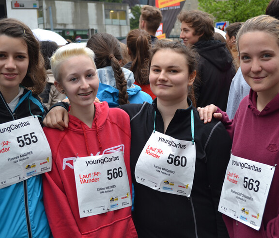 Vier junge Erwachsene Frauen stehen zusammen  zu einem Gruppenfoto. Sie nehmen alle an einem Laufwettbewerb teil und tragen Wettkampfnummern. 