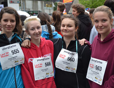 Vier junge Erwachsene Frauen stehen zusammen  zu einem Gruppenfoto. Sie nehmen alle an einem Laufwettbewerb teil und tragen Wettkampfnummern. 