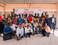Viele Erwachsene aus dem Südsudan stehen vor der Schule in Gumbo vor einem Plakat, auf dem steht "Welcome Caritas Austria Team".