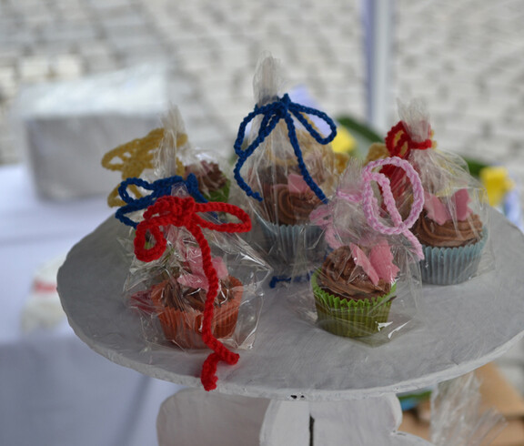 Auf einem hölzernen Hocker, der weiß angestrichen wurde, stehen verpackte kleine Schokomuffins. Zusammengebunden wurde die Verpackung mit großen bunten Schleifen. 