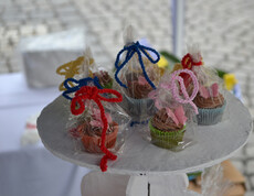 Auf einem hölzernen Hocker, der weiß angestrichen wurde, stehen verpackte kleine Schokomuffins. Zusammengebunden wurde die Verpackung mit großen bunten Schleifen. 