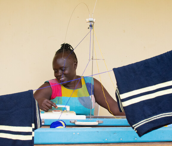 Eine Schwarze Frau sitzt lächelnd an einer Nähmaschine und arbeitet.