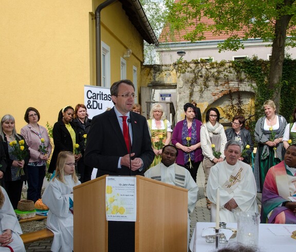 Bürgermeister von St. Pölten spricht ins Mikrofon und hinter ihm stehen Frauen mit gelben Rosen