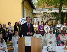 Bürgermeister von St. Pölten spricht ins Mikrofon und hinter ihm stehen Frauen mit gelben Rosen