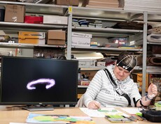 Frau zeichnet in einem Atelier ein Bild und ist von technischen Geräten umgeben.