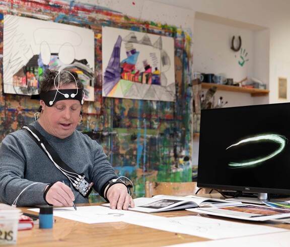 Mann in einem Künstleratelier beim Zeichnen umgeben von einer technischen Ausrüstung.