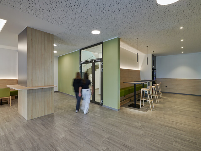 Innenansicht Aula Caritas Schule Wiener Neustadt, 2 Mädchen gehen zur Glastür Richtung Stiegenhaus