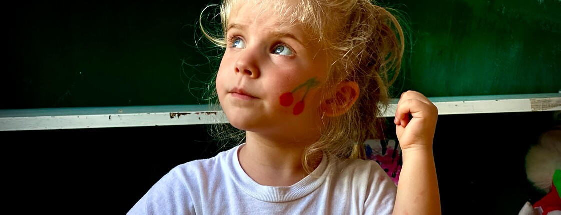 Blondes Mädchen mit Kirschmotiv auf der Wange nimmt am Kinderprogramm in Puka, Albanien, teil