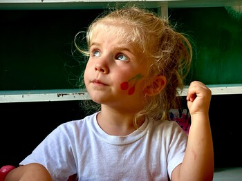 Blondes Mädchen mit Kirschmotiv auf der Wange nimmt am Kinderprogramm in Puka, Albanien, teil