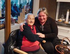 Zwei Personen sitzen eng beieinander, festliche Deko und weitere Gäste im Hintergrund