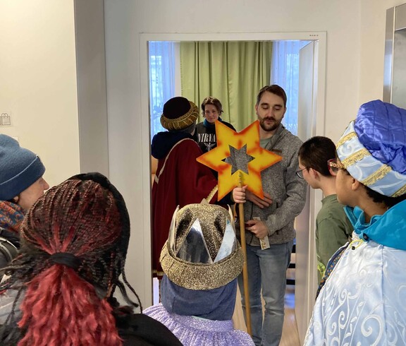 Familie öffnet drei Kindern, die als Sternsinger unterwegs sind, die Tür.