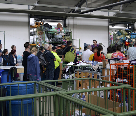 Führung durch das Kleidersortierwerk von carla. Menschen gehen durch enge gänge, die von Wagen voller Kleider geformt werden. 