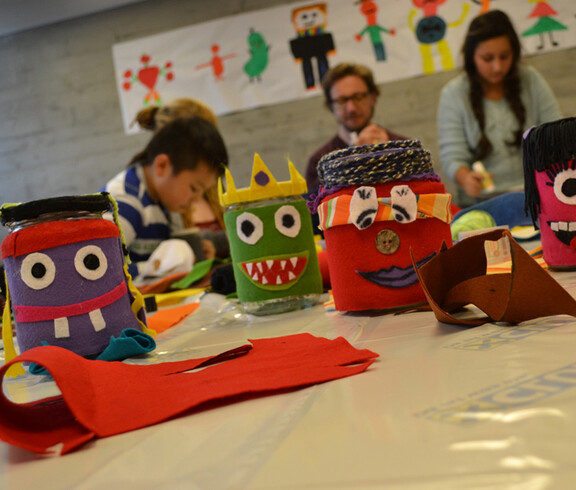 Verzierte, farbige Spendengläser. Man hat den Gläsern Gesichter aufgeklebt.  Siie sind mit Stoff umhüllt und wurden im Lerncafe Lustenau aufgestellt. 