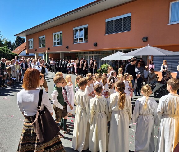 Vor dem Pflegewohnhaus versammelt sich eine große Prozession mit Kindern und Gottesdienstgestaltung, um gemeinsam eine feierliche Andacht im Freien zu feiern.