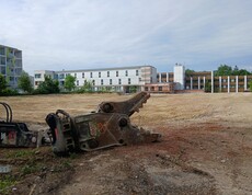 Blick auf eine Baufläche im Vordergrund ein Baggerteil