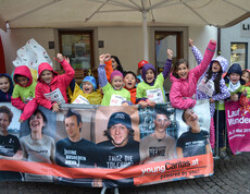 Eine Ansammlung von Kindern befindet sich in der feldkircher Innenstadt. Sie alle nehmen teil an einem Laufwettbewerb. Alle haben sie Wettkampfnummern und stehen hinter Gittern.  