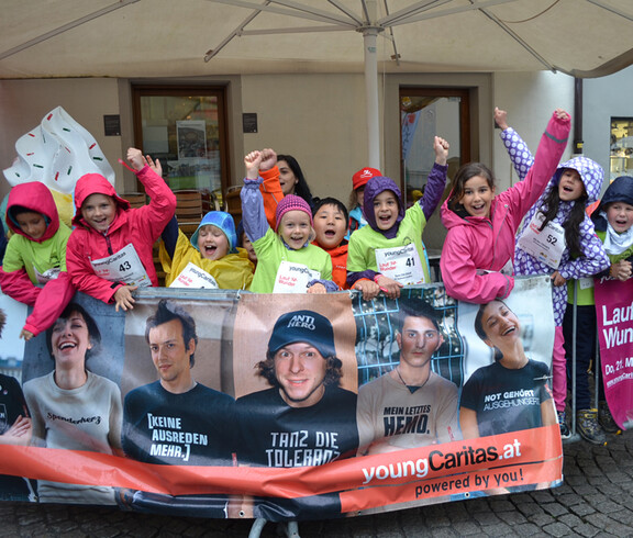 Eine Ansammlung von Kindern befindet sich in der feldkircher Innenstadt. Sie alle nehmen teil an einem Laufwettbewerb. Alle haben sie Wettkampfnummern und stehen hinter Gittern.  