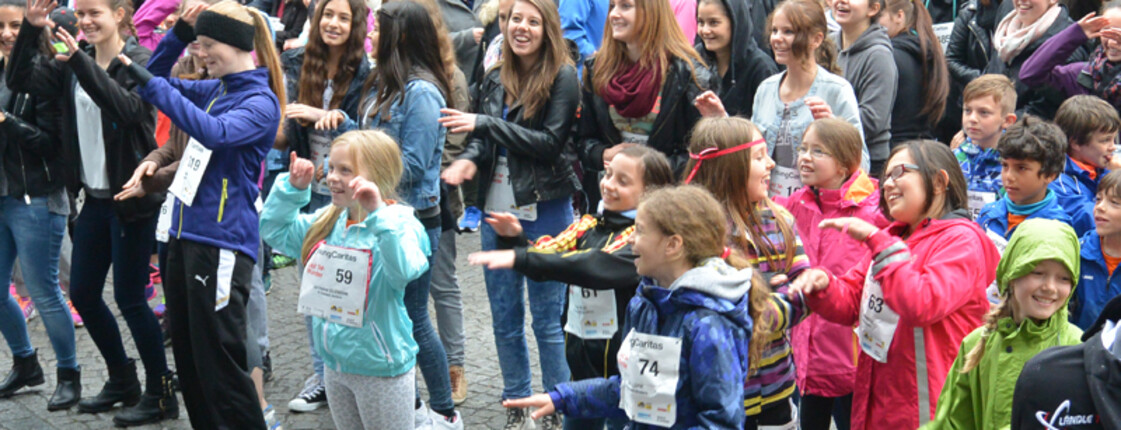 Eine große Ansammlung von Jugendlichen befindet sich in einer Innenstadt. Sie alle nehmen teil an einem Laufwettbewerb. Alle haben sie Wettkampfnummern. 