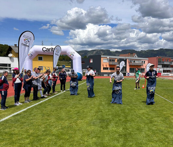 Teilnehmende absolvieren ein Sackhüpfen auf dem Sportplatz, begleitet von Zuschauer*innen beim Teamtag.