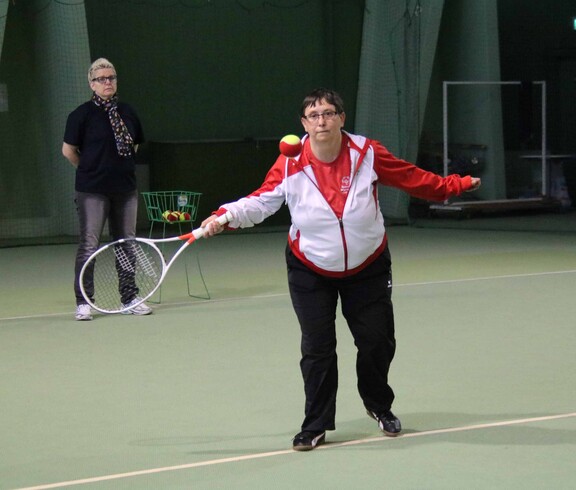 Frau in rotweissrotem Trikot mit Tennisschläger in Action