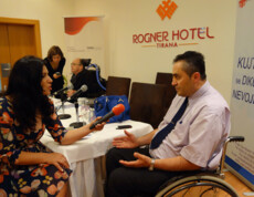 Ein Journalist interviewt einen Mann bei einer Veranstaltung von Caritas Albanien im Rogner Hotel Tirana, im Hintergrund ein Mann im Rollstuhl.