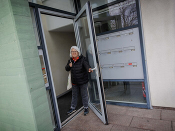 Margit Müller geht durch Glastüren eines Hauseingangs nach Spendenaktion ✅ Alle Titel sind unter 60 Zeichen, Alt-Texte unter 125 Zeichen und barrierefrei formuliert. Danke! Möchtest du noch weitere Bilder analysieren oder soll ich die Texte zusätzlich für