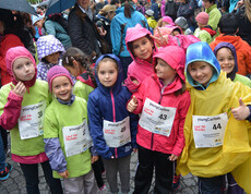 Etliche kleine Kinder nehmen bei einem Laufwettbewerb in der feldkircher Innenstadt teil. Sie tragen alle Startnummern, die jeweils an der Brust befestigt wurden, und unterschliedlich farbige Regenjacken und Trikots. 