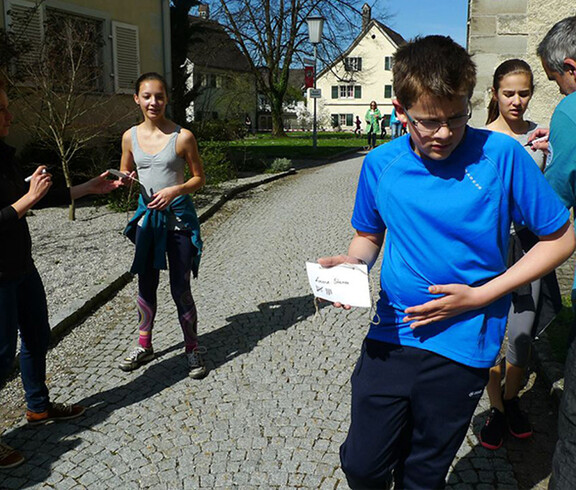 Den Läuferinnen wird ein Strich auf ihre Laufnummer gemacht. Die Sonne scheint.