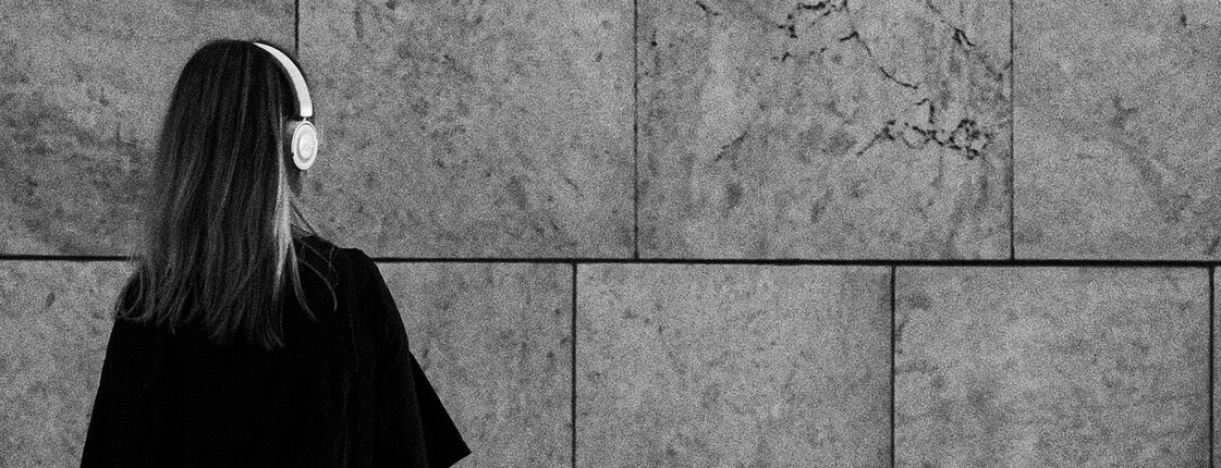 Jugendliche Person mit Kopfhörern steht allein vor einer Steinwand, Sinnbild für Rückzug und Einsamkeit im Jugendalter.