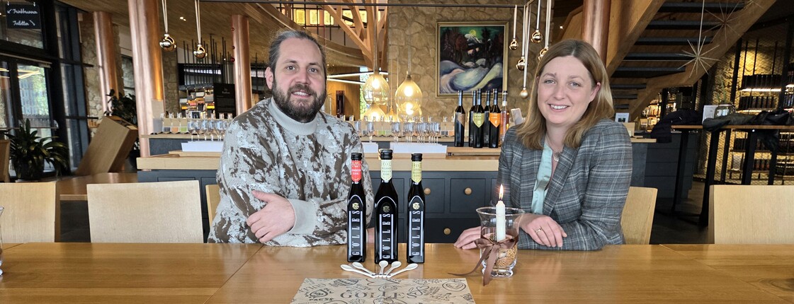 David Gölles & Nora Tödtling-Musenbichler, Direktorin Caritas Steiermark sitzen vor den Essigen von Gölles