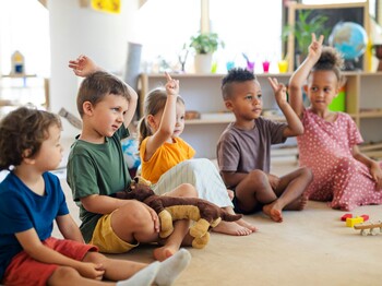 Kinder sitzen in einer Gruppe in einem Kreis und melden sich mit der Hand.