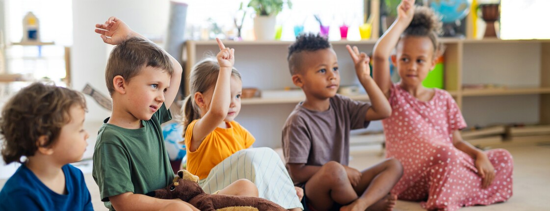 Kinder sitzen in einer Gruppe in einem Kreis und melden sich mit der Hand.