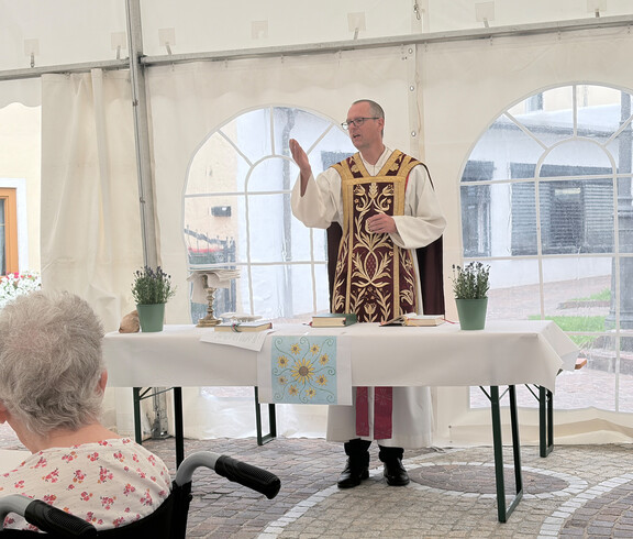 Geistlicher spricht bei der Heiligen Messe im Festzelt des Sommerfests vor den Gästen von Haus Theresia.