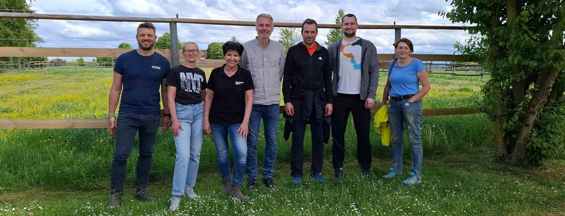 Gruppe steht in der Wiese vor einer Koppel