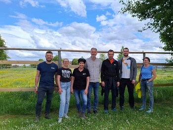 Gruppe steht in der Wiese vor einer Koppel