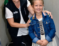 Ein kleines junges Mädchen trägt ein Kleid. Hinter ihr steht eine Frau mittleren Alters, die für Carla arbeitet.