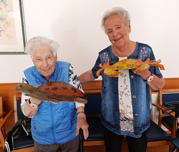 Zwei Bewohnerinnen halten fertig gestaltete Papiermaché-Figuren wie Schildkröte und Krabbe in den Händen.