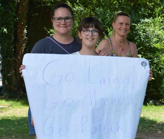 Drei Mädchen feuern eines beim Go Kart Rennen mit einem Plakat an 