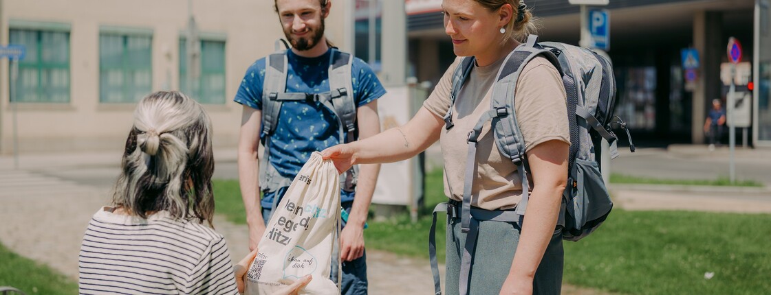 Zwei Streetworker*innen der Caritas Bahnhofsmission übergeben ein Hitzeschutzpaket