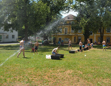 Wasserfontäne auf Wiese, im Hintergrund viele Kinder in Badebekleidung