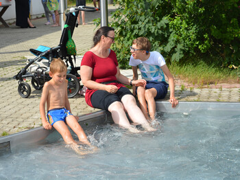 Frau und zwei Kinder sitzen am Poolrand und halten die Füße hinein