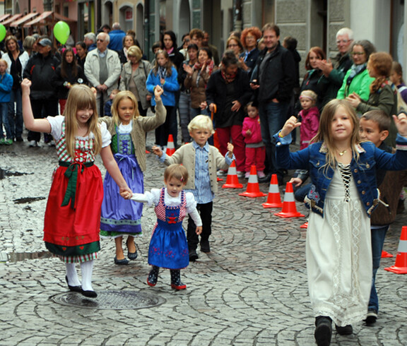 Kinder in Tracht laufen durch die feldkircher Innnenstadt. Sie sind dabei von Erwachsenen umbgeben, die zusehen. 