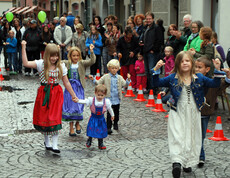 Kinder in Tracht laufen durch die feldkircher Innnenstadt. Sie sind dabei von Erwachsenen umbgeben, die zusehen. 