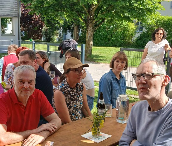 Viele Personen sitzen an Bierbänken im Garten