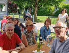Viele Personen sitzen an Bierbänken im Garten