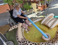 Eine Bewohnerin eines Pflegewohnhauses kühlt ihre Füße in einem Planschbecken und übt dabei spielerisch Geschicklichkeit mit verschiedenen Wasserutensilien.